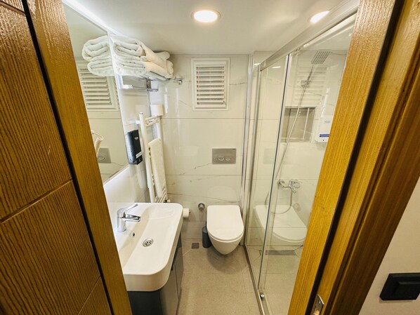 A compact bathroom with a sink, toilet, and glass shower enclosure. - YAKIN PANSİYON (Amasra)
