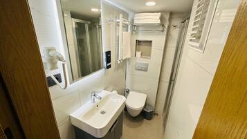 A compact bathroom with a sink, toilet, and shower.