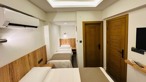 Een hotelkamer met een lange gang, bedden met een houten hoofdbord, een airconditioning, een houten deur en een televisie aan de muur.