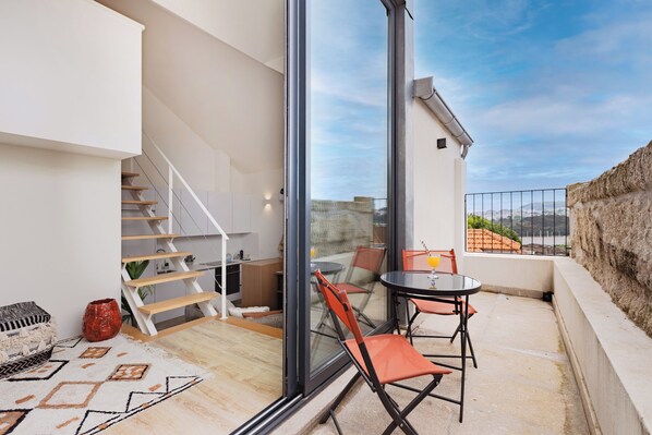 A modern interior with a staircase, a dining area with chairs and a table, and a view through a large window. - Saldanha Boho Duplex (Porto)