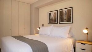 A neatly made bed with a grey throw blanket, a bedside lamp, and two framed pictures on the wall. - w* | Enchanting 1BR w/Balcony in San Isidro (San Isidro)