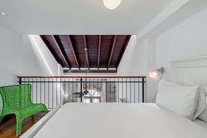 Ein Schlafzimmer mit Bett, einem grünen Sessel, einem Balkon mit Aussicht und einer Deckenleuchte.