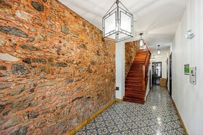 A hallway with a stone wall, a wooden staircase, patterned floor tiles, and a hanging light fixture. - w* | Classy 1BR in Plaza Herrera w/ Balcony (Panamá)