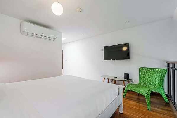 Habitación de hotel con cama, escritorio, silla, televisor y aire acondicionado.