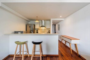 Una cocina moderna con una isla central, dos taburetes y una mesa de madera.