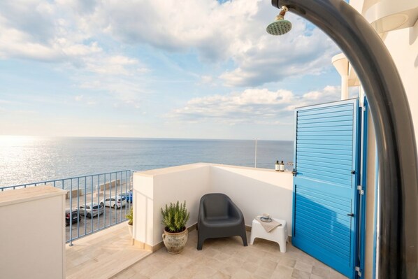 Un balcón con vistas al mar, una silla, una mesita, una planta en maceta y una puerta azul.