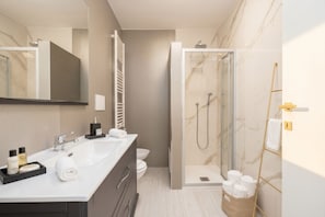 Un baño moderno con un espejo grande, ducha, inodoro y tocador con artículos de aseo.