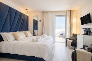 Una habitación de hotel moderna con una cama grande, un televisor de pantalla plana, un escritorio con cafetera y vistas al exterior.