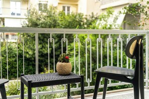 Egy balkon, melyen virágtartóban kaktusz, egy fonott asztal és egy fekete szék található.