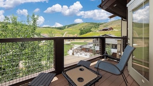 A balcony with a view of a green landscape and a building in the distance. - Cozy Condo: Ski In/Out with Slopeside Views at Base Camp One (Granby)