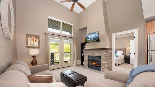 A spacious living room with a fireplace, a large window, and a ceiling fan. - Cozy Condo: Ski In/Out with Slopeside Views at Base Camp One (Granby)