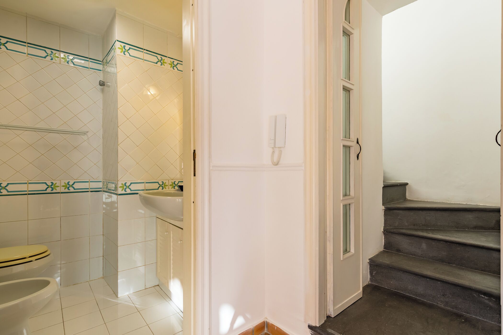 A bathroom with a toilet, sink, and shower. There is a phone on the wall and a door leading to a staircase.