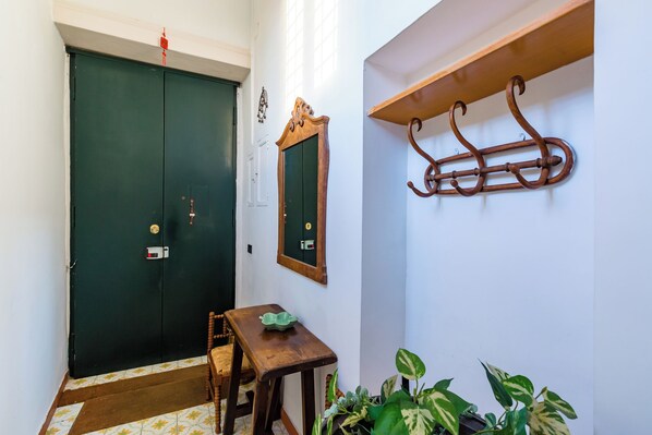 A room with a green door, a small wooden table with a green bowl, a chair, a mirror, and a coat rack with a coat. - Villa Paola - Hidden Panoramic Garden and Terraces by Napoliapartments (Naples)