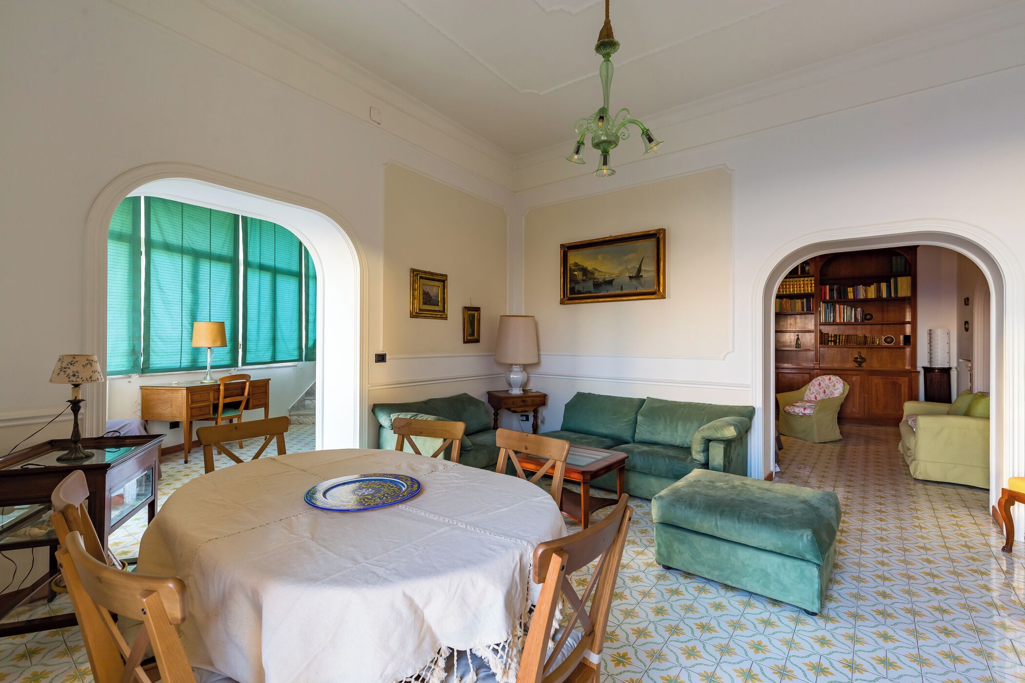 A cozy living room with a round table, green sofas, and a bookshelf.