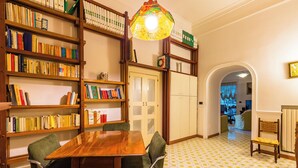 A room with a wooden dining table, green upholstered chairs, and a bookshelf filled with books. - Villa Paola - Hidden Panoramic Garden and Terraces by Napoliapartments (Naples)