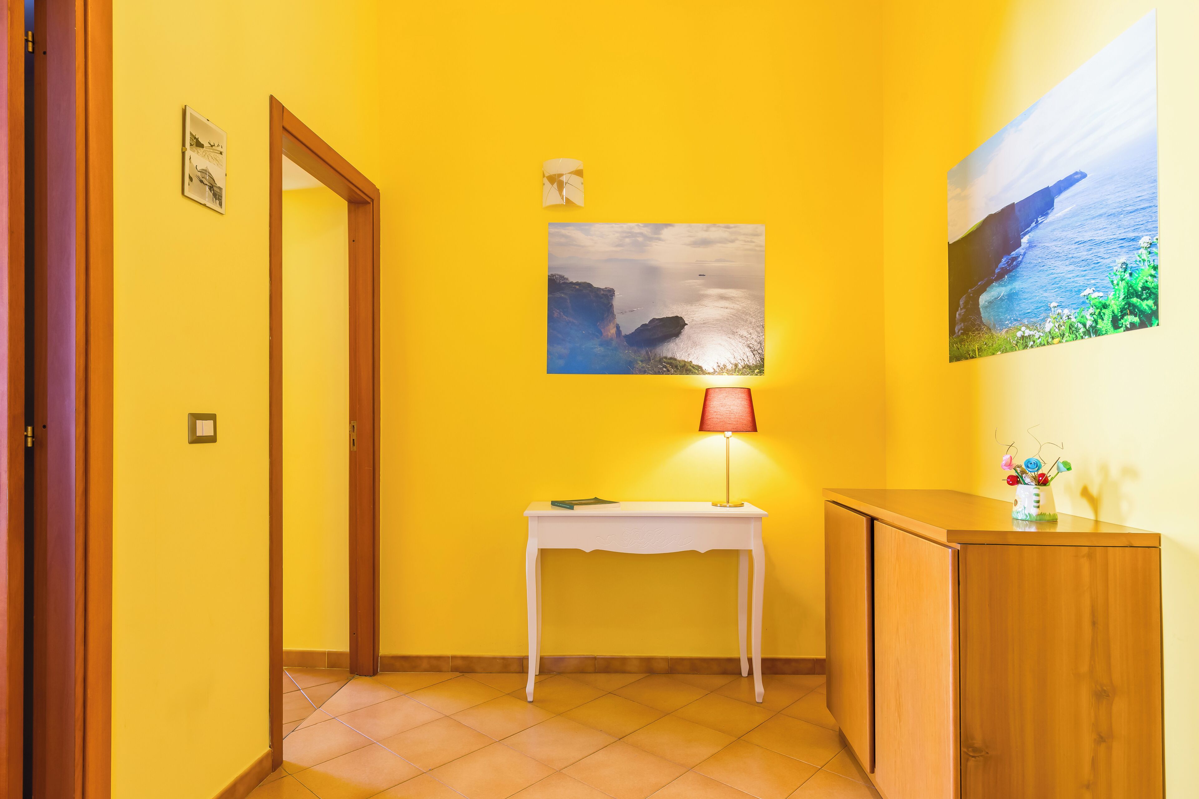 A hallway with a white table, a lamp, and a painting of a cliff.