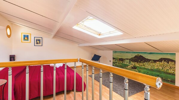 A bedroom with a red bed, a skylight, a painting of a town, and a wooden railing. - Terrazza San Paolo by Napoliapartments (Naples)