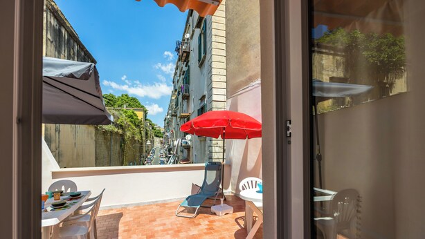 A balcony with a table, chairs, and a red umbrella. - Terrazza Spaccanapoli by Napoliapartments (Naples)
