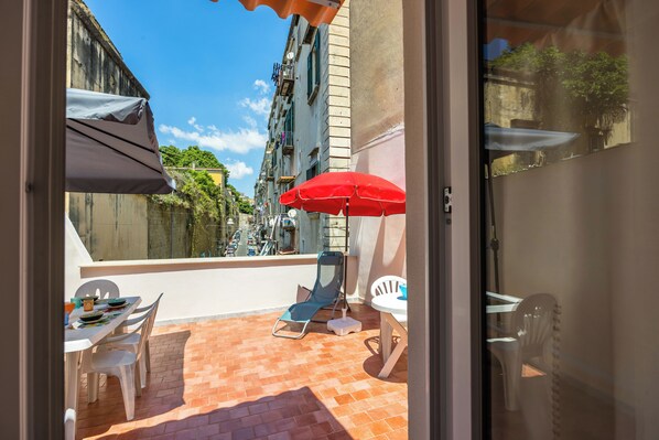 Un balcon avec une table, des chaises et un parasol rouge.