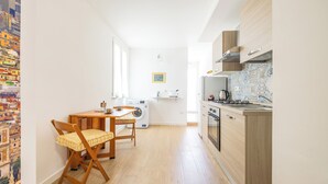 Une cuisine compacte équipée d’un lave-linge, d’une table à manger avec des chaises, et offrant une vue sur une fresque colorée sur le mur de gauche.