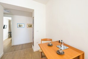 Een eethoek met een houten tafel, twee stoelen, een koffiepot en een kopje op een schotel. Twee ingelijste foto's hangen aan de muur.