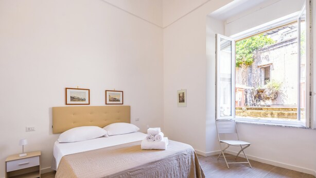 Une chambre d’hôtel avec un lit, une table de chevet, une chaise et une fenêtre donnant sur des immeubles.