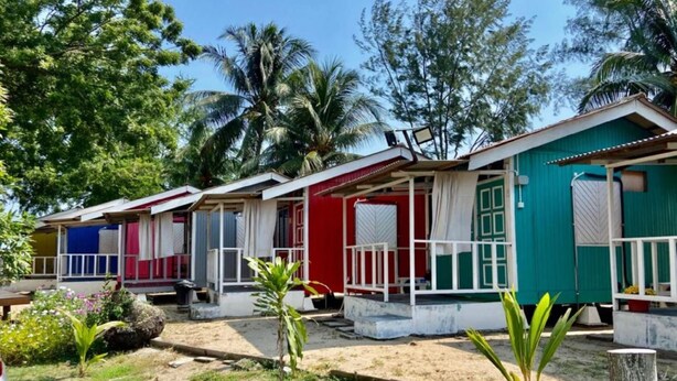 A row of colorful, single-story cabins with white railings, surrounded by greenery and palm trees. - Global Star Chalet (Malacca City)