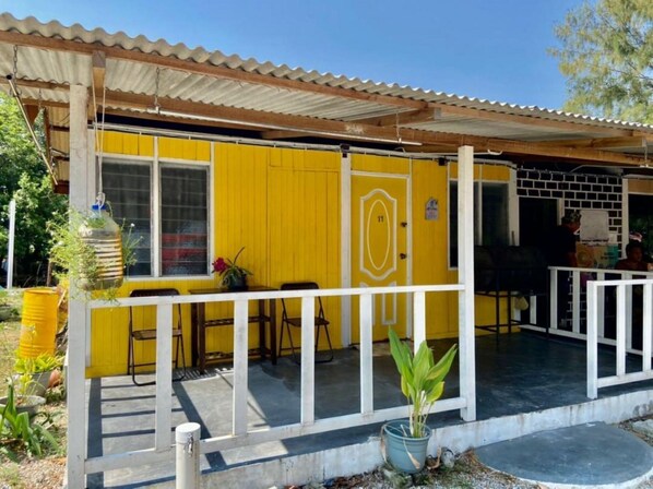 Ein gelbes Gebäude mit überdachter Veranda, der Hausnummer 11 und Sitzgelegenheiten im Freien.