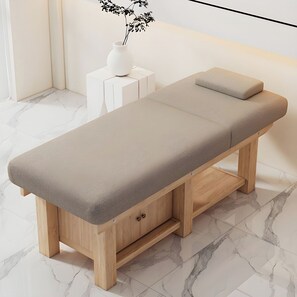Mesa de massagem de madeira com apoio para a cabeça acolchoado e gavetas de armazenamento, posicionada sobre um chão de mármore em um ambiente minimalista.