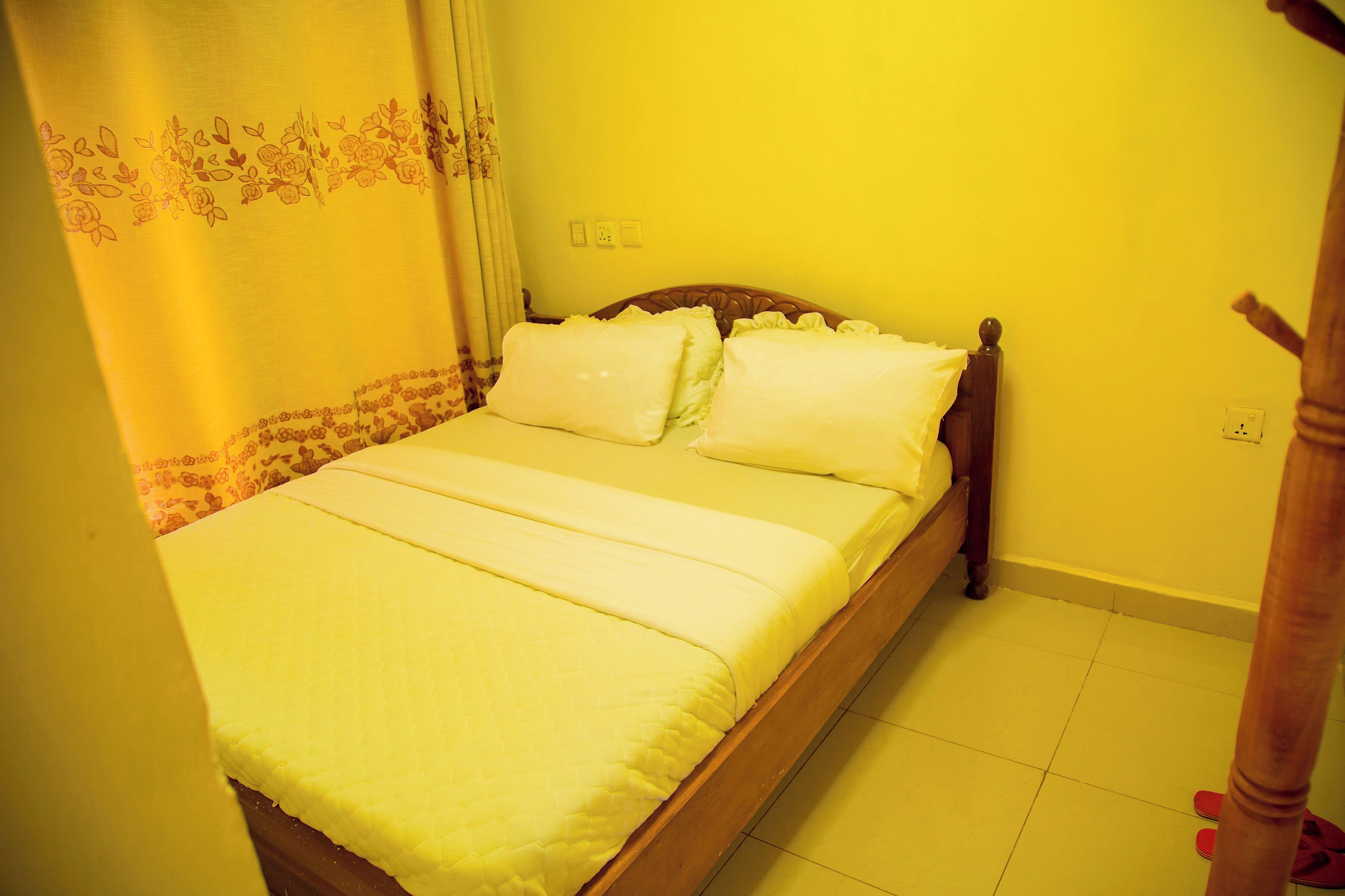 A bed with a wooden frame, white bedding, and a floral curtain.
