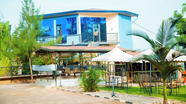 A modern building with a blue and white exterior, a balcony, and outdoor seating areas with umbrellas. - Novaland Hotel Rw (Kigali)