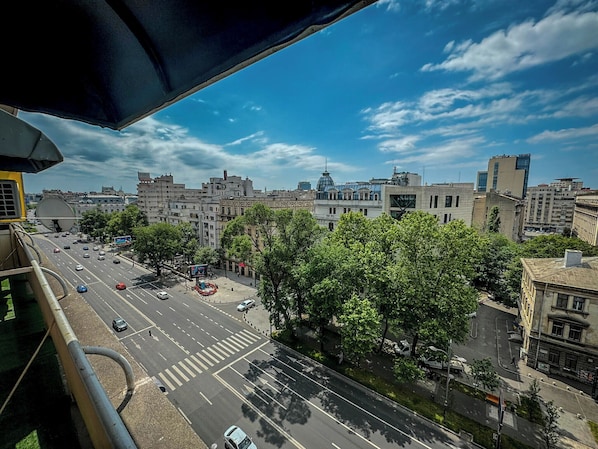 Stadtansicht mit blauem Himmel, einem markanten Kuppelgebäude und einer belebten Straße mit Autos und Bäumen.