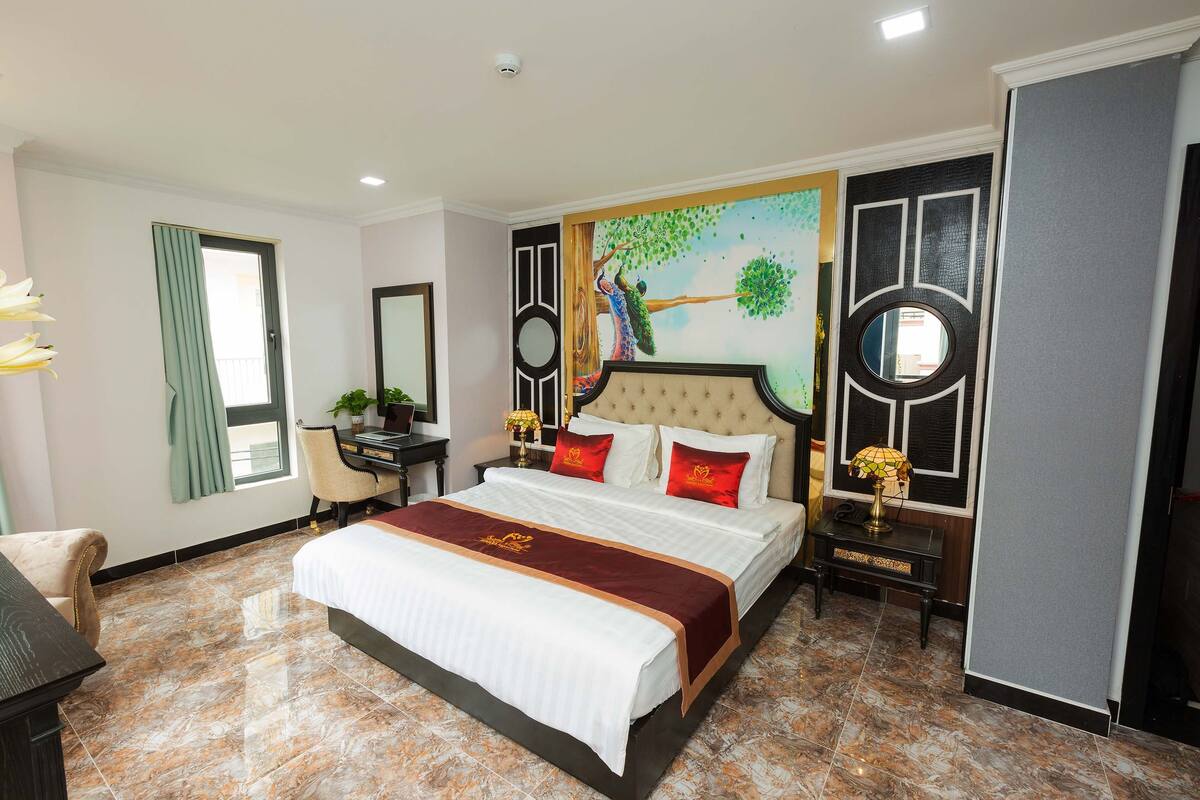 A hotel room with a large bed, a desk, a chair, and a window with curtains.