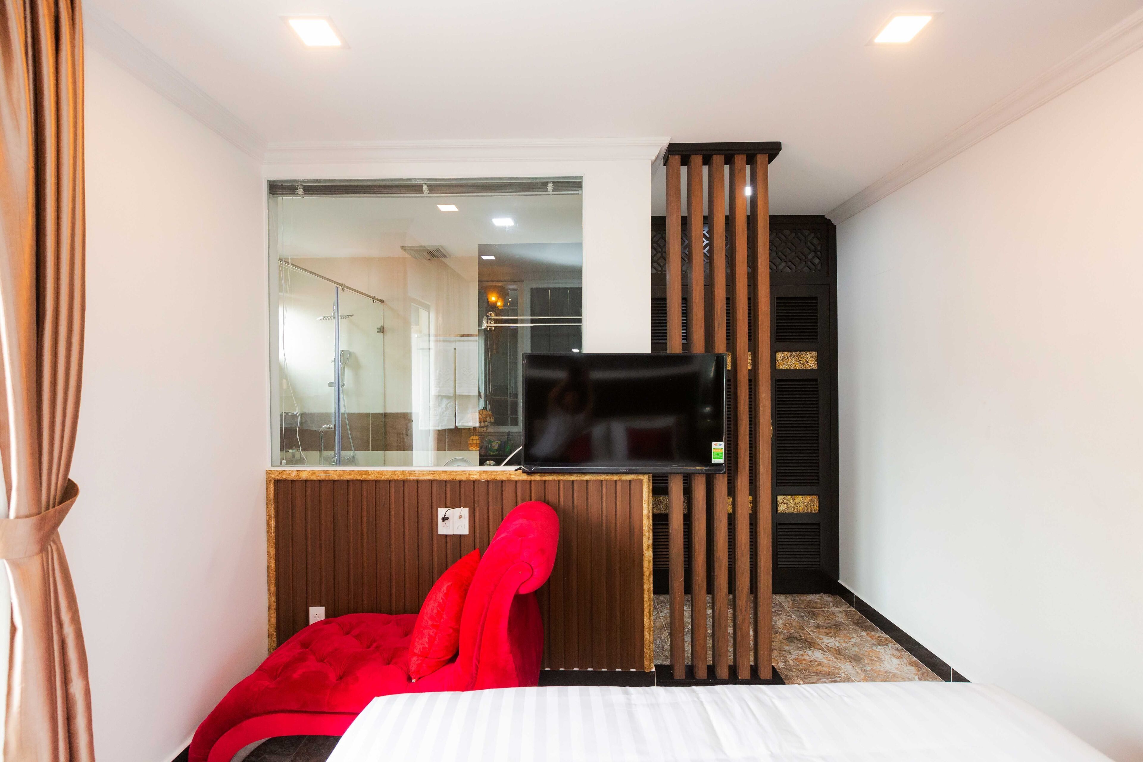 A hotel room with a bed, a red chair, a TV, and a glass shower enclosure.