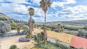 A residential property with a car parked in front, a red-roofed building, and palm trees.
