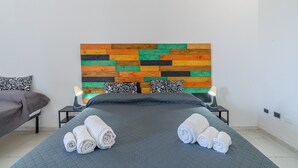 Een opgemaakt bed met opgerolde handdoeken, een hoofdbord met een kleurrijk houten patroon en twee bedlampen.