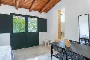 Ein Zimmer mit Holzboden, einem Esstisch mit Stühlen, einem kleinen weißen Hocker und einer grünen Tür mit Fenstern.