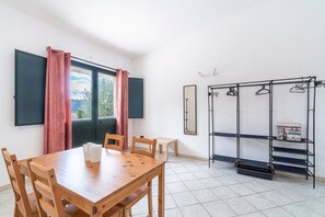 Une pièce comprenant une table à manger en bois, des chaises, une petite table blanche, une étagère en métal avec des porte-manteaux et une fenêtre avec des rideaux.