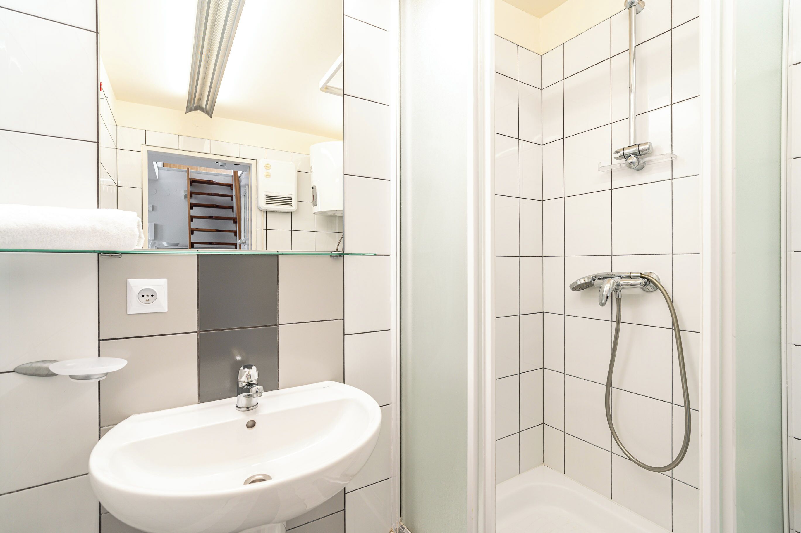 A modern bathroom with a white sink, glass shelf, and a shower with a handheld showerhead.