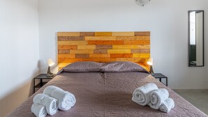 A bed with a wooden headboard, two bedside lamps, and rolled towels on the bed. - Studio 'Origano - Fiumara Val Di Noto' with Mountain View, Wi-Fi and Air Conditioning (Noto)