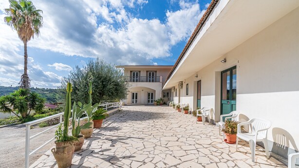 A stone-paved courtyard with potted plants, white chairs, and a building with a balcony. - Studio 'Origano - Fiumara Val Di Noto' with Mountain View, Wi-Fi and Air Conditioning (Noto)