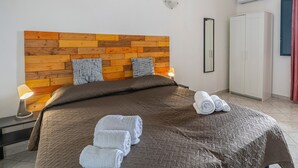Une chambre à coucher avec une tête de lit en bois, deux lampes de chevet, une armoire et des serviettes soigneusement pliées sur le lit.