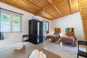 A hotel room with wooden ceiling beams, a large wardrobe, two beds with towels, a chair, and a view of greenery outside.