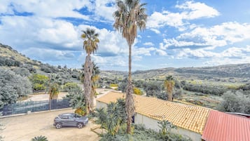 A residential property with a car parked in front, a red-roofed building, and palm trees.