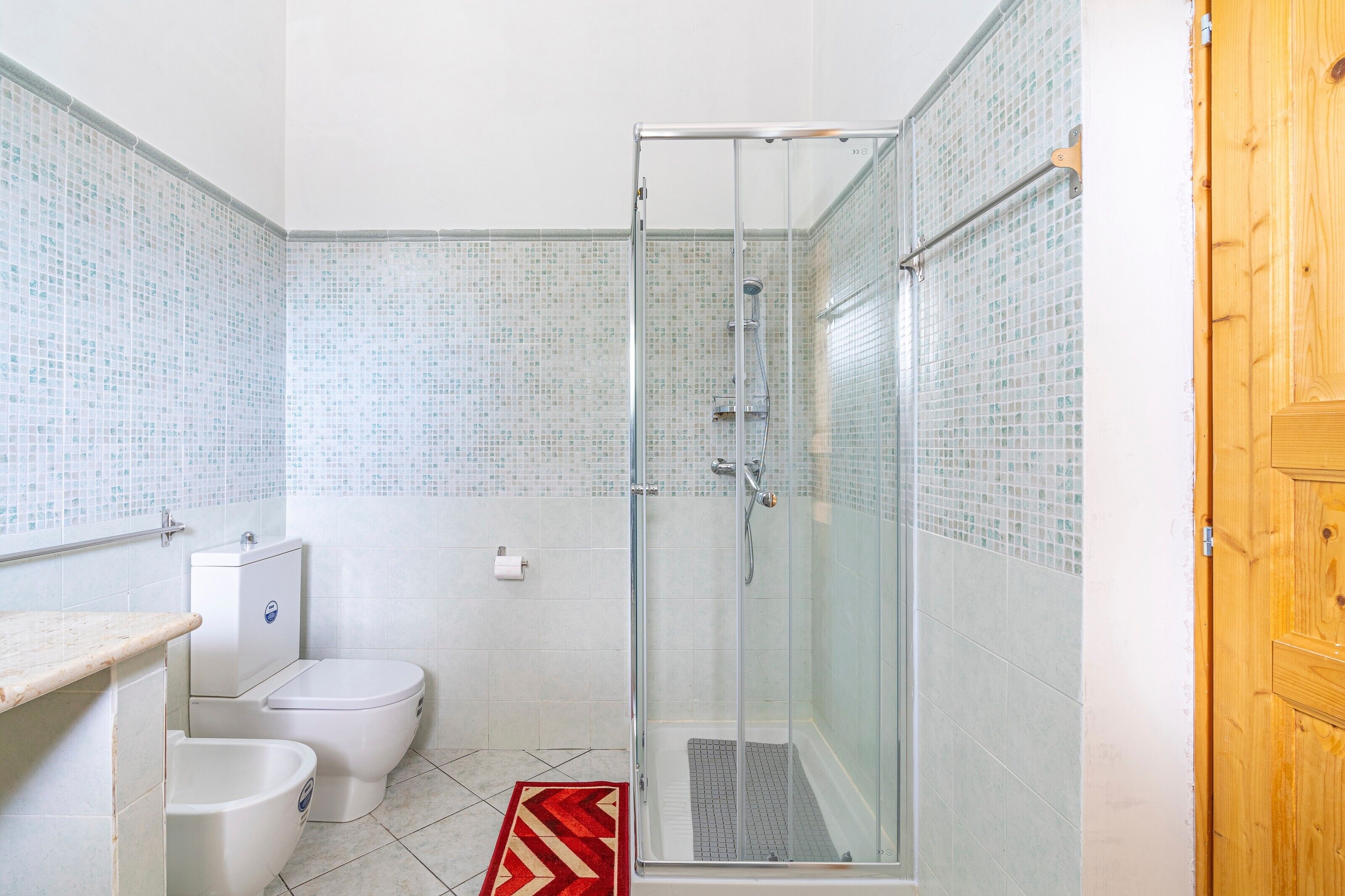 A bathroom with a shower, toilet, bidet, and tiled walls.