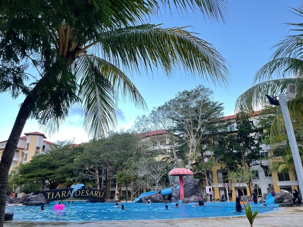 Zona de piscina con tobogán y palmeras.