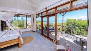Una habitación amplia con una cama grande, una terraza de madera y vista al mar.