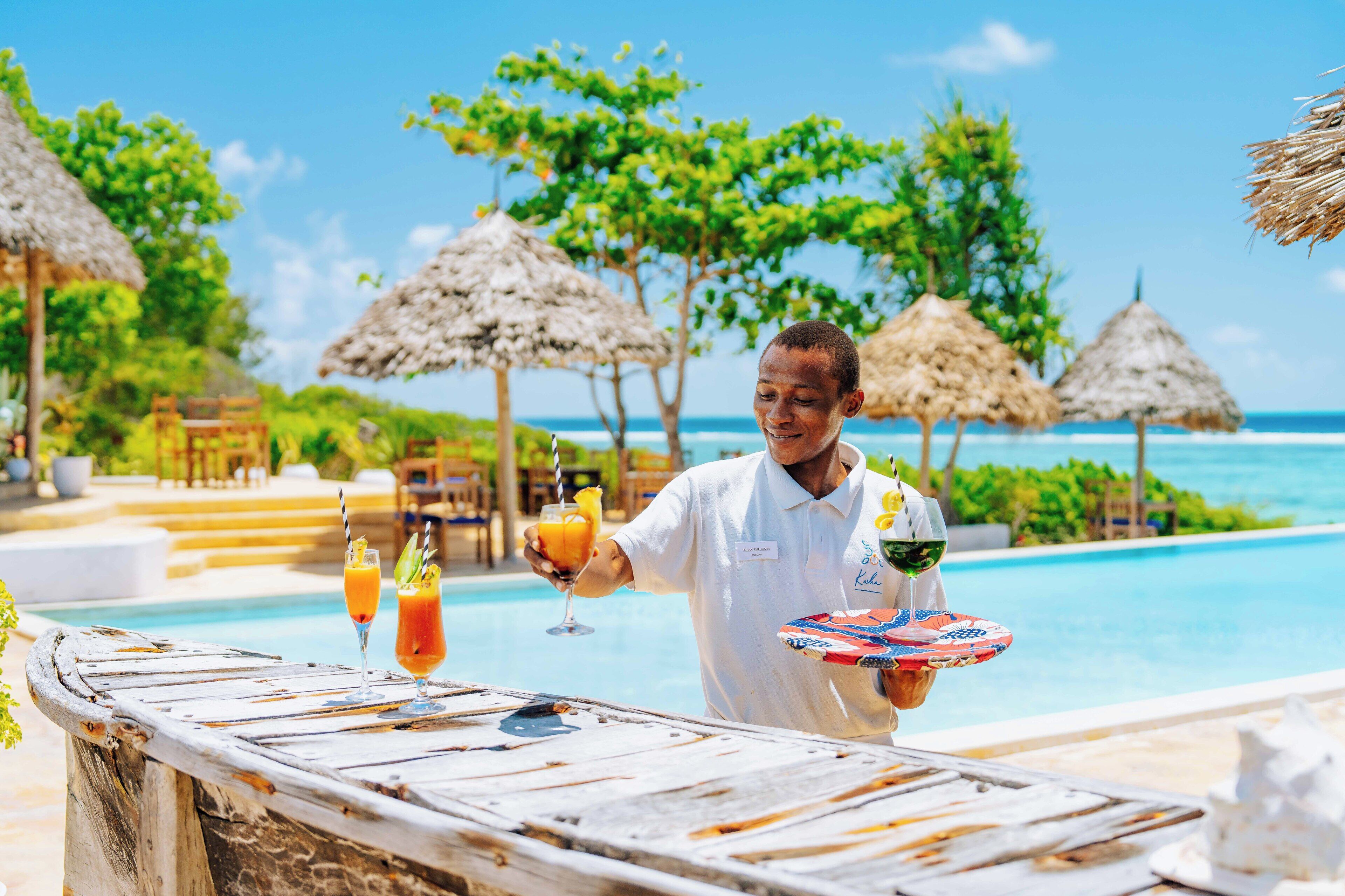A poolside bar with tropical drinks and a person holding a tray.