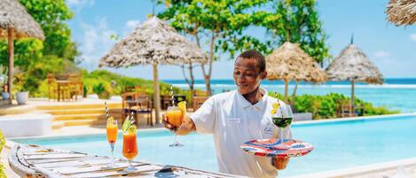 A poolside bar with tropical drinks and a person holding a tray.