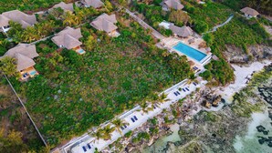 Vista aérea de un resort con villas de techo de paja, una piscina y una zona de playa.